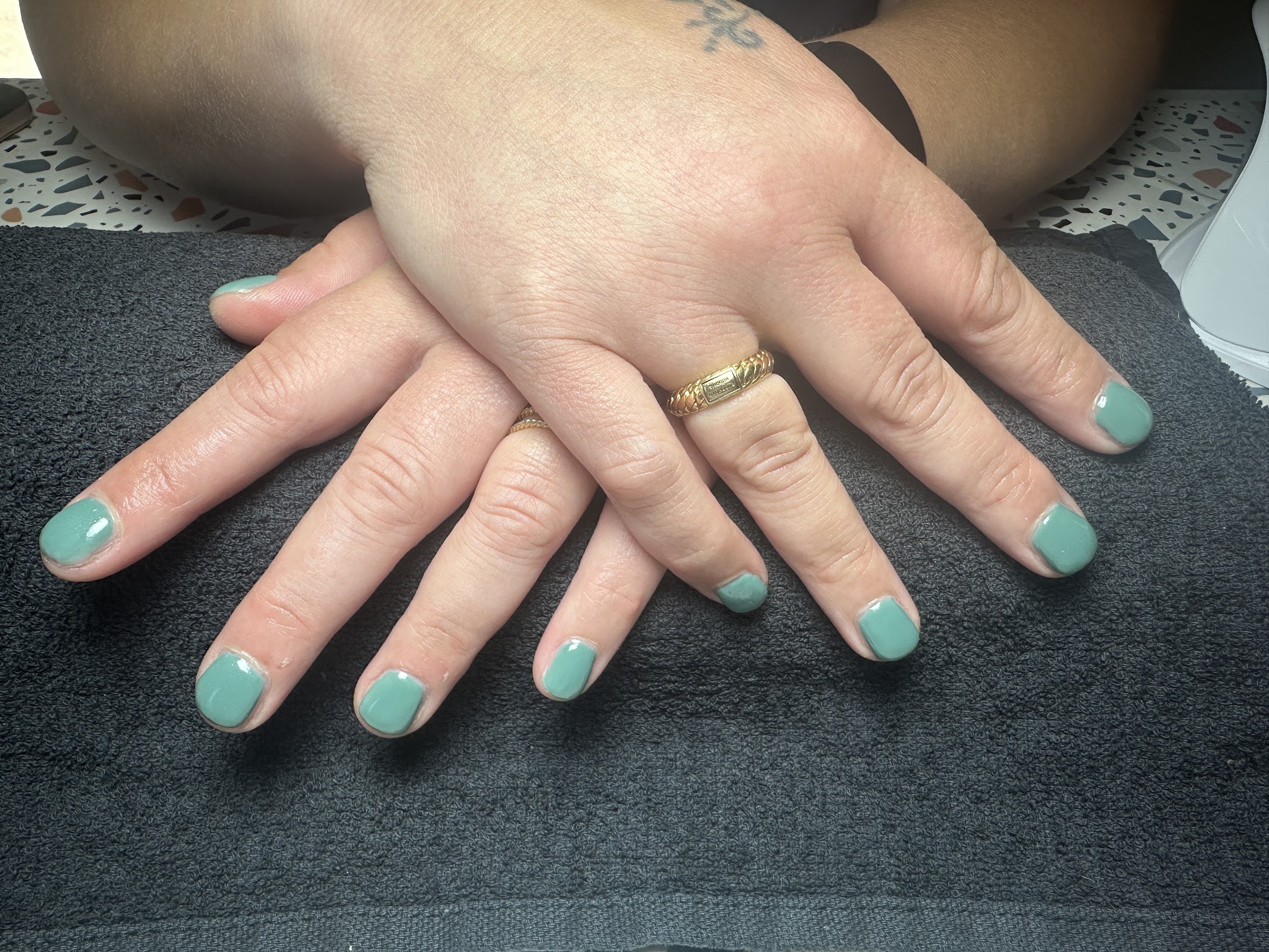 Twee handen met saliegroene gelnagels op een grijze handdoek