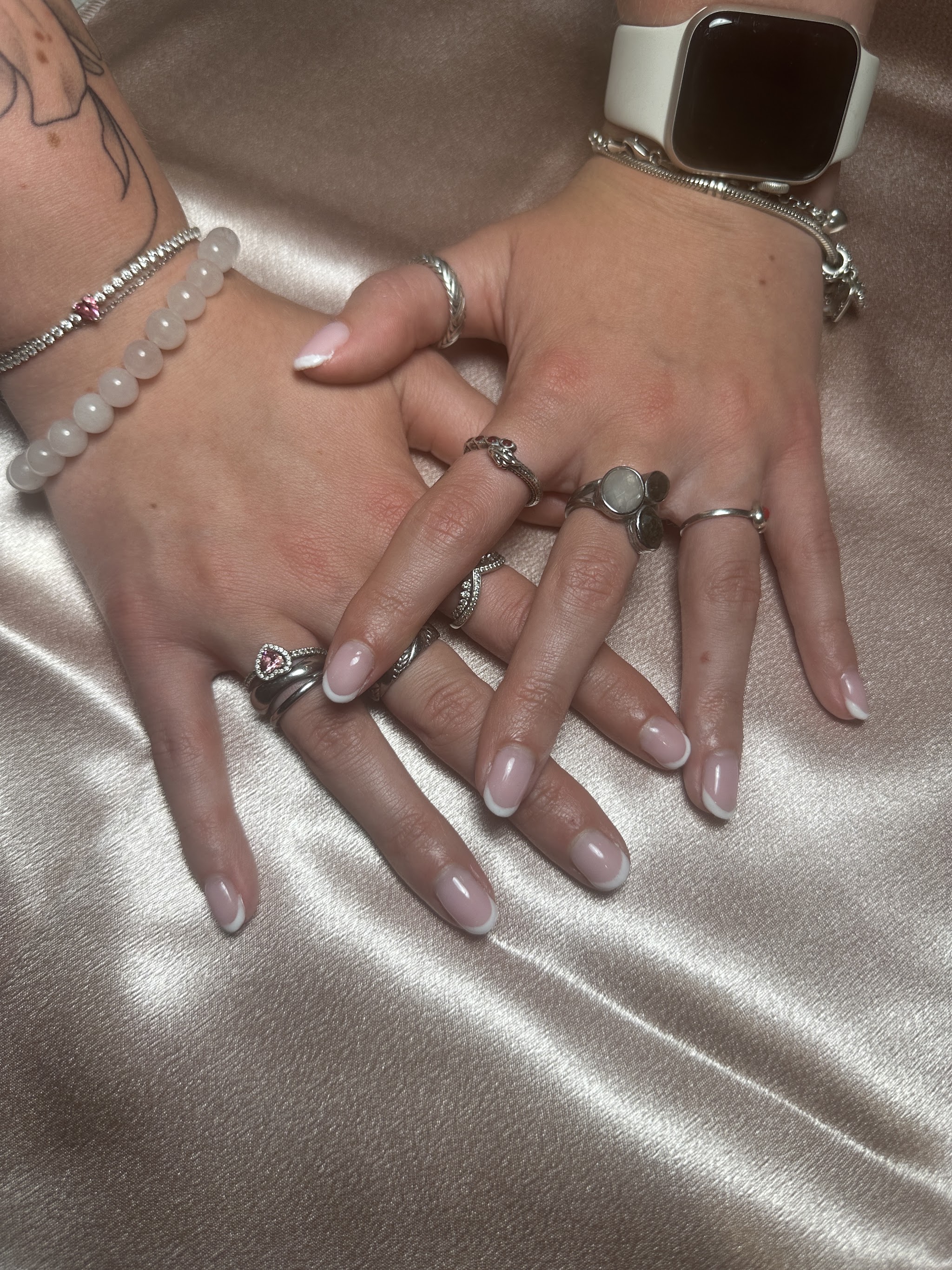 Hand met naturel nagels en zilveren ringen op satijn