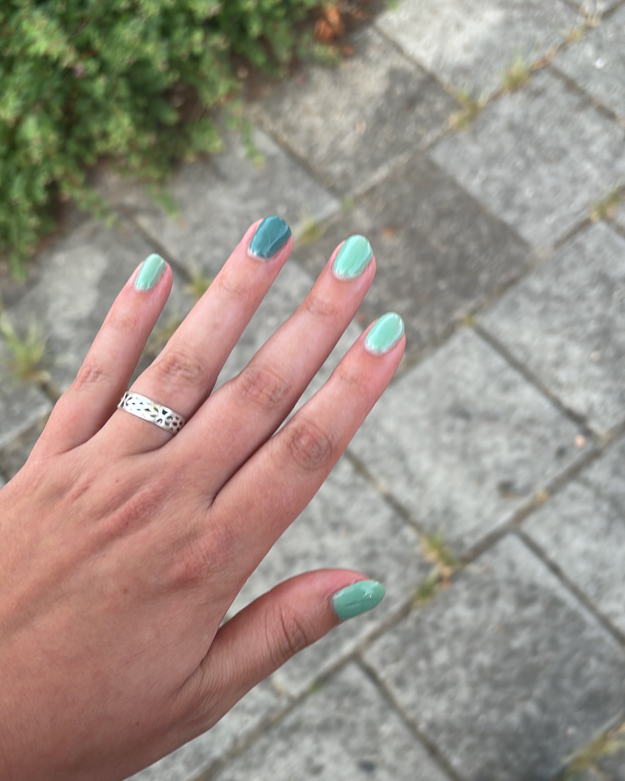 Hand met turquoise nagels en een zilveren ring, buiten op de stoep